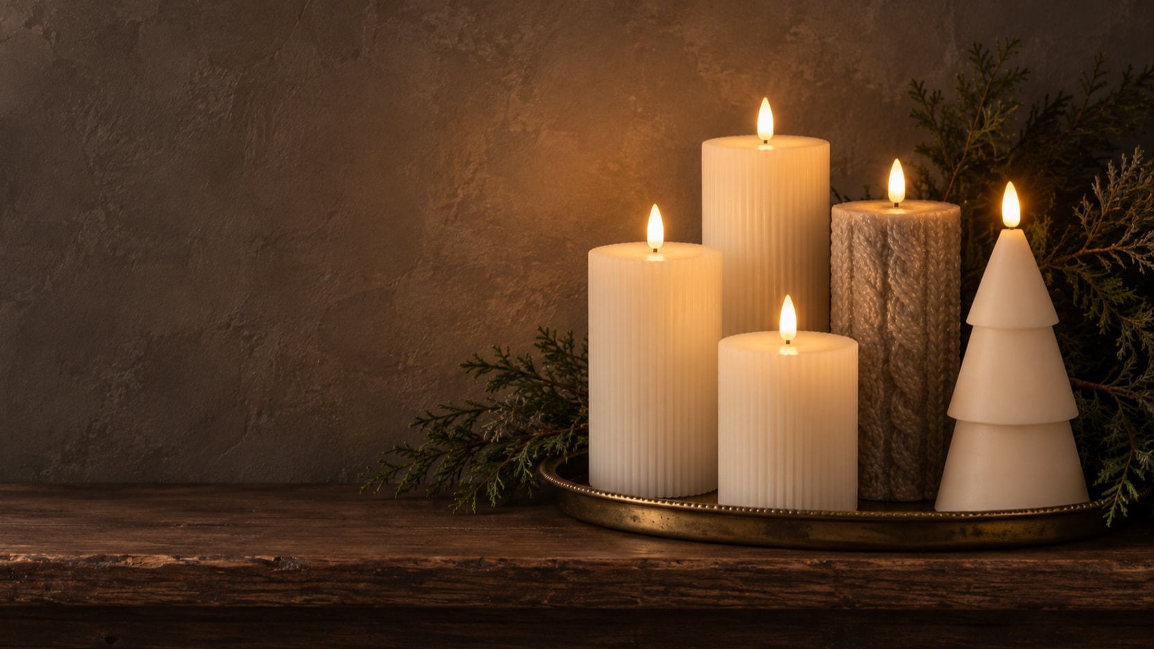 Cream grooved pillars, a taupe cable-knit candle, and a cream tree candle grouped on a brass tray with cedar, all lit